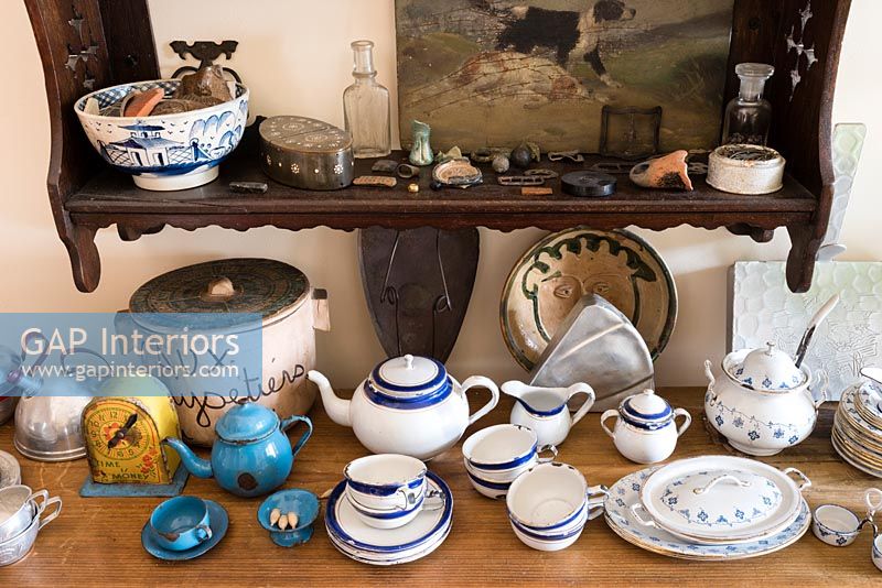 Crockery on wooden sideboard with shelf of ornaments above 