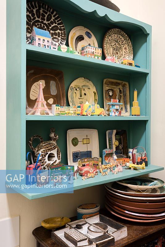 Blue wall mounted shelves covered in plates and small ornaments 