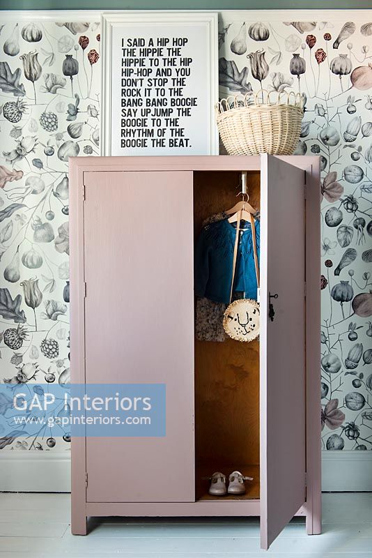 Dusky pink painted wardrobe in childrens bedroom with floral wallpaper 