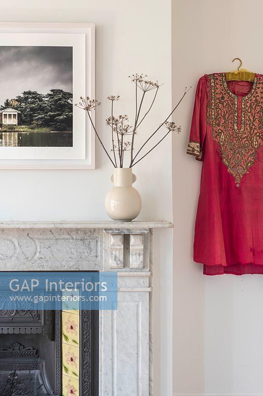 Bright red Indian style dress on wall of living room next to fireplace 