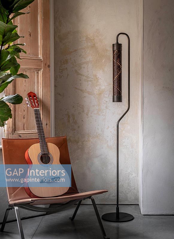 Guitar on leather chair next to modern floor lamp in living room