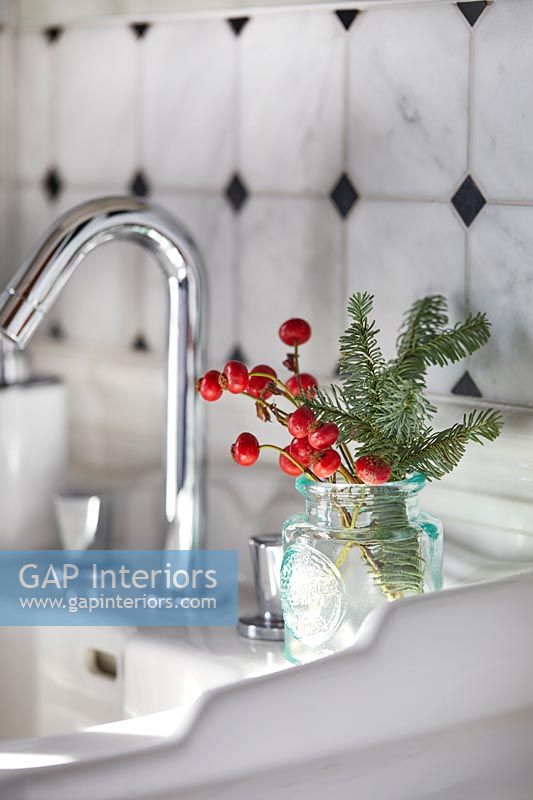 Pine tree foliage and red berries in glass jar next to sink 