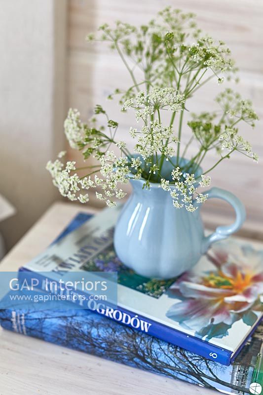Pale blue jug of cut wild flowers on bedside table with books 