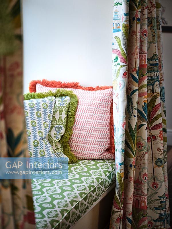 Patterned fabric covered cushions and curtains on window seat 