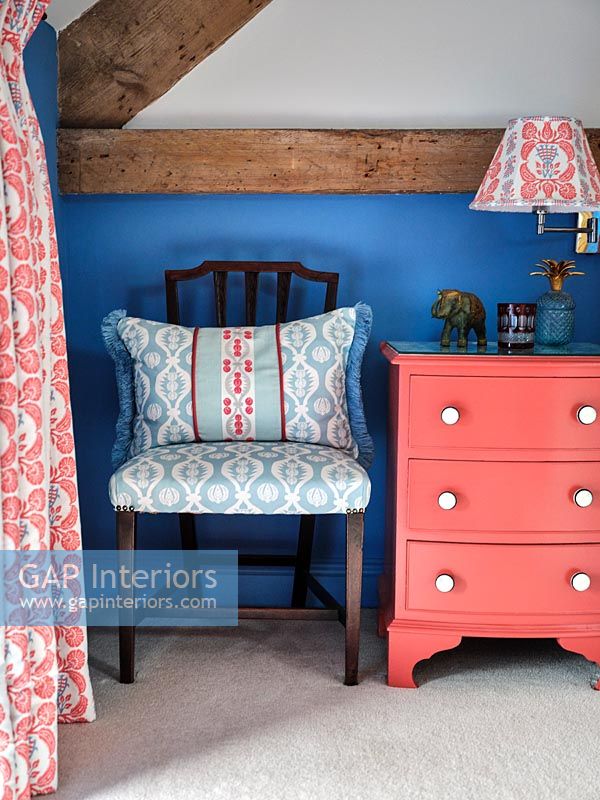 Pink painted bedside cabinet against blue painted wall in country bedroom