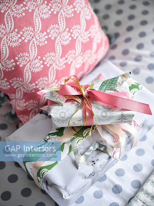 Wrapped gifts on bed next to patterned cushions 