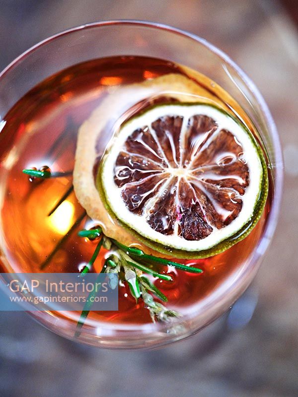detail of spiced drink with slice of dried lime and sprig of rosemary 