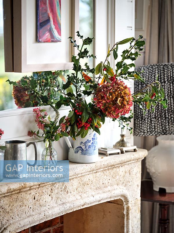 Flower and foliage arrangement in jug on mantelpiece 