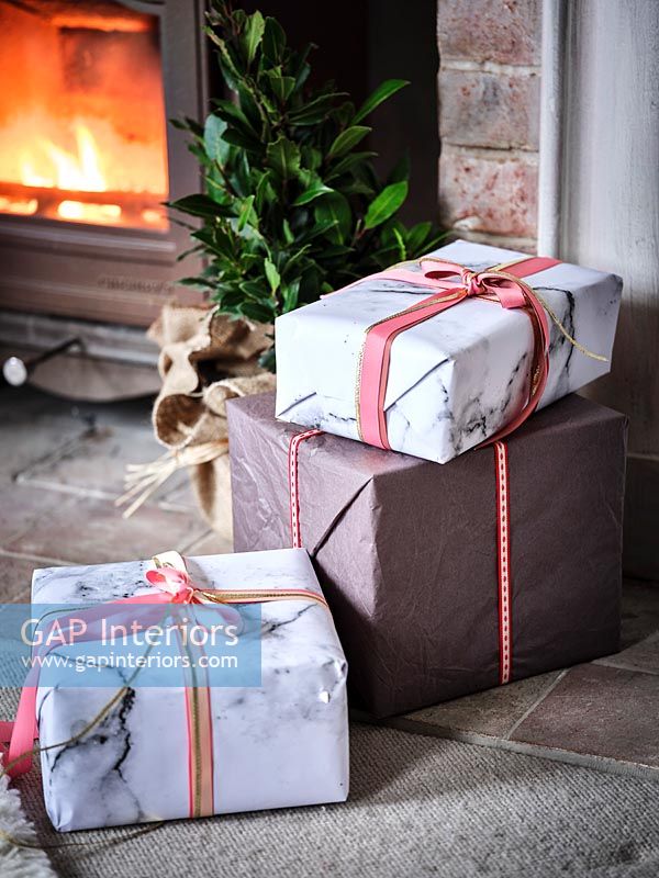 Detail of wrapped Christmas gifts next to lit wooden burning stove 