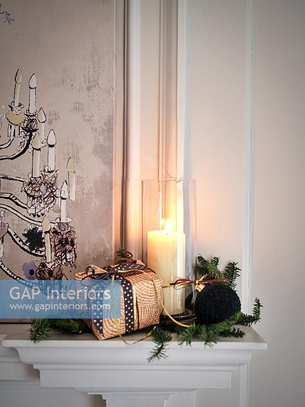 Christmas gift, decoration and lit candle on mantelpiece 