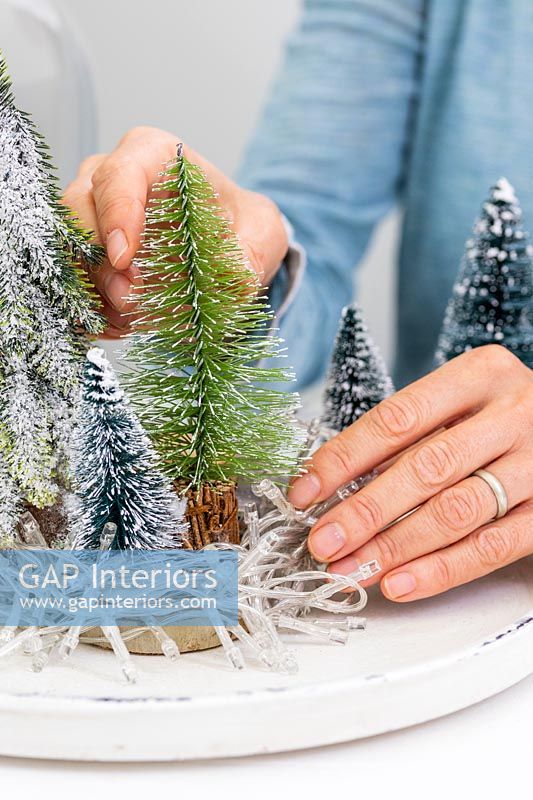 Woman adding fake miniature christmas trees to tray
