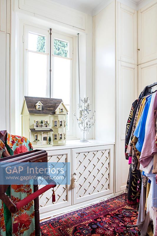 Dolls house on windowsill and colourful clothing hanging on clothes rail