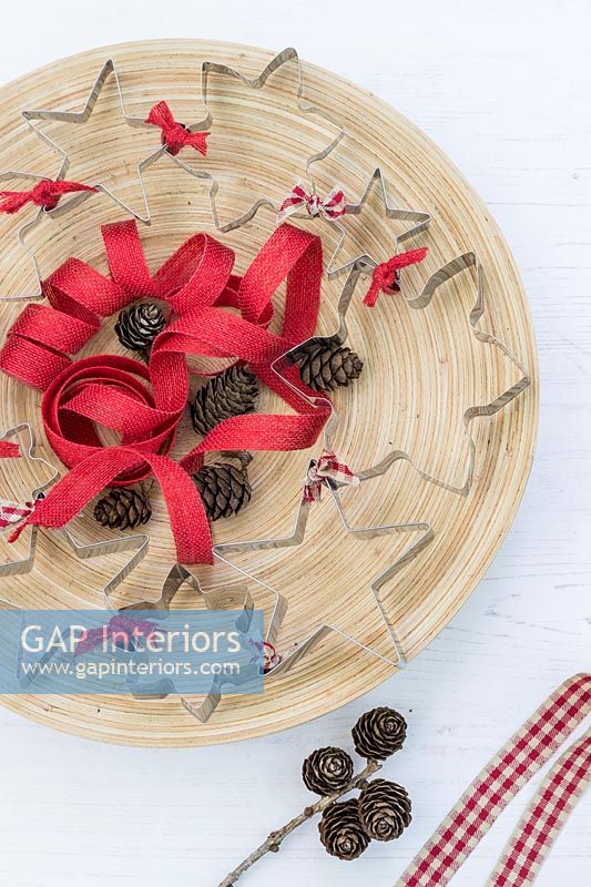 Wreath made from cookie cutters tied together with red ribbon, placed on a wooden tray