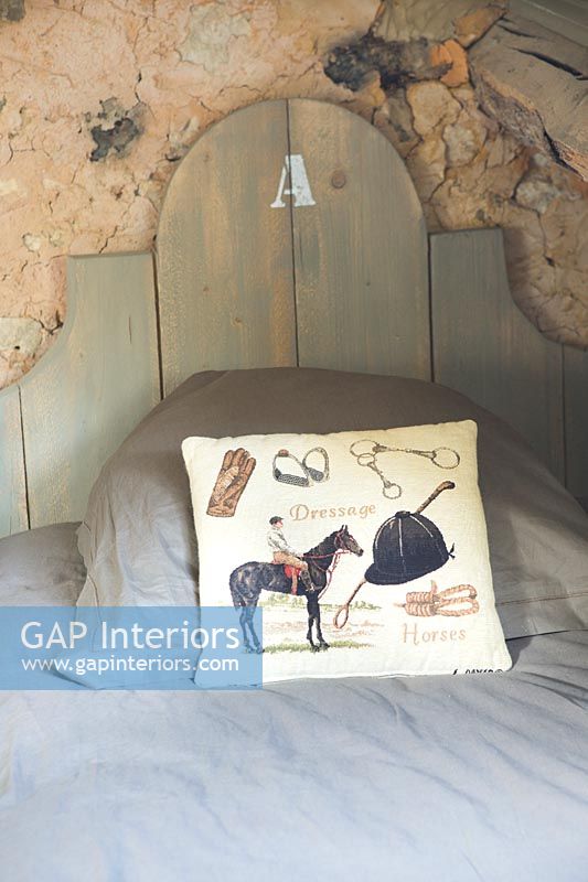 Equestrian themed cushion on bed with exposed stone wall behind 