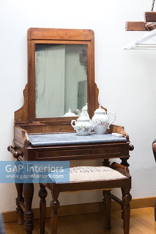 Tiny wooden dressing table, mirror and stool in country bedroom 