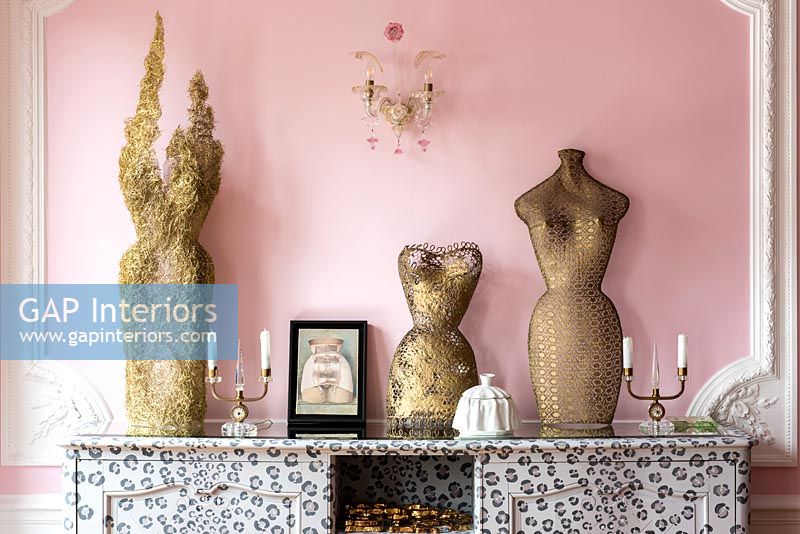 Golden sculptures against pink wall in eclectic living room 