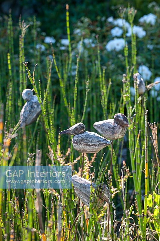 Bird ornaments among long grass in country garden 