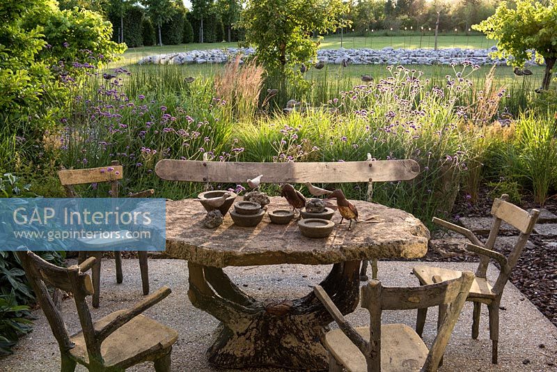 Rustic table and chairs on terrace overlooking country garden in summer 