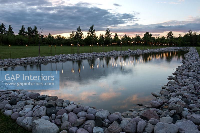 Water feature lined with pebbles and decorative lights in evening 