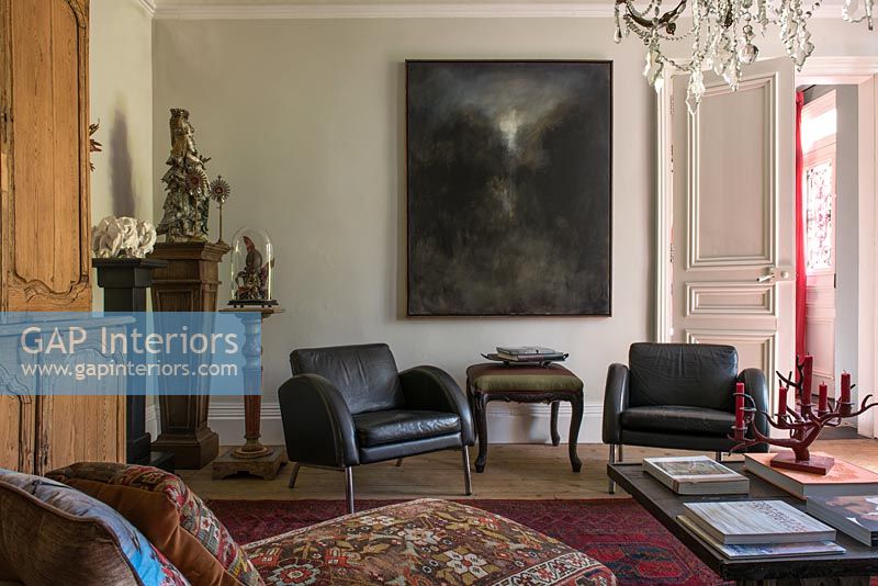 Pair of black leather chairs under dark painting in living room 