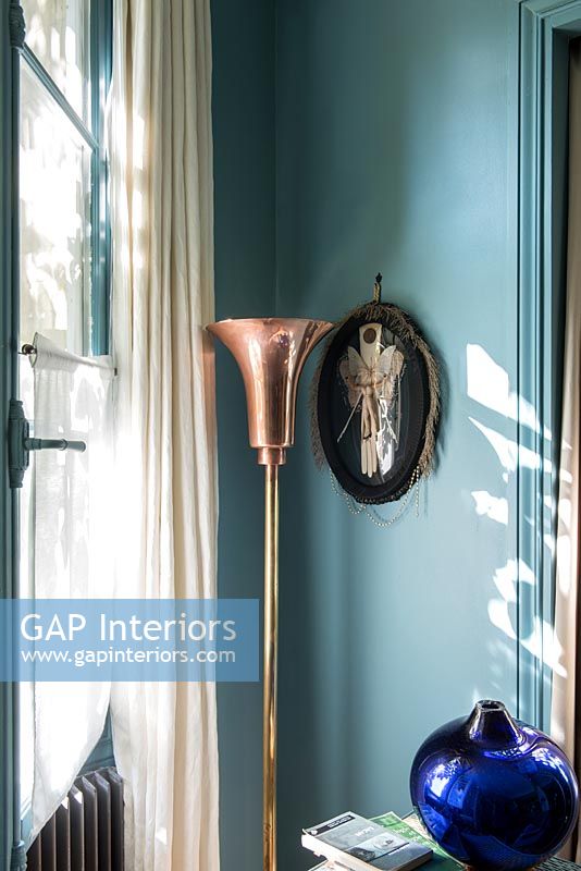 Decorative copper floor lamp and fabric picture on blue painted wall