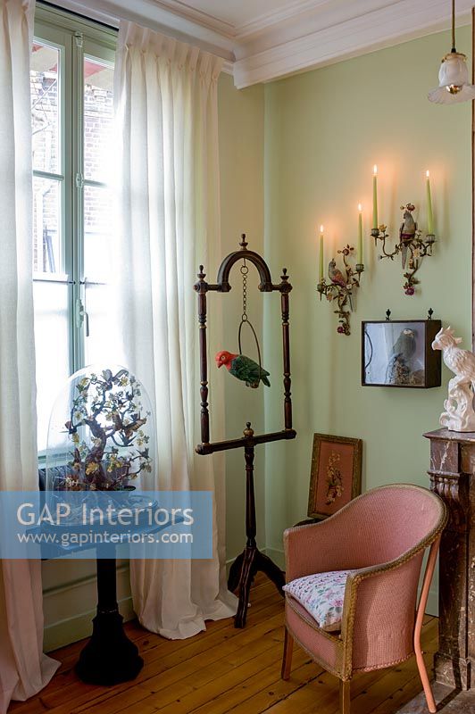 Green painted wall and pink antique chair surrounded by ornaments 