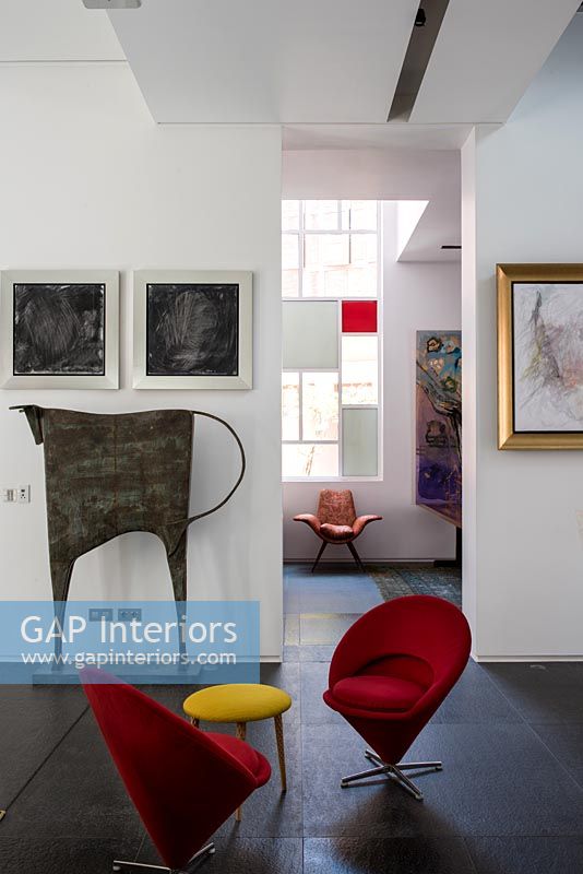 Small red chairs with yellow stool side table surrounded by modern artwork 