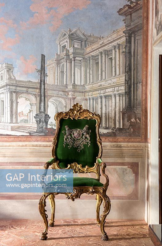 Green velvet gilded chair next to fresco wall 