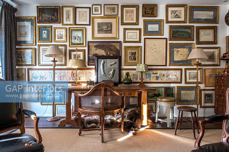 Feature wall display of framed paintings in country study 
