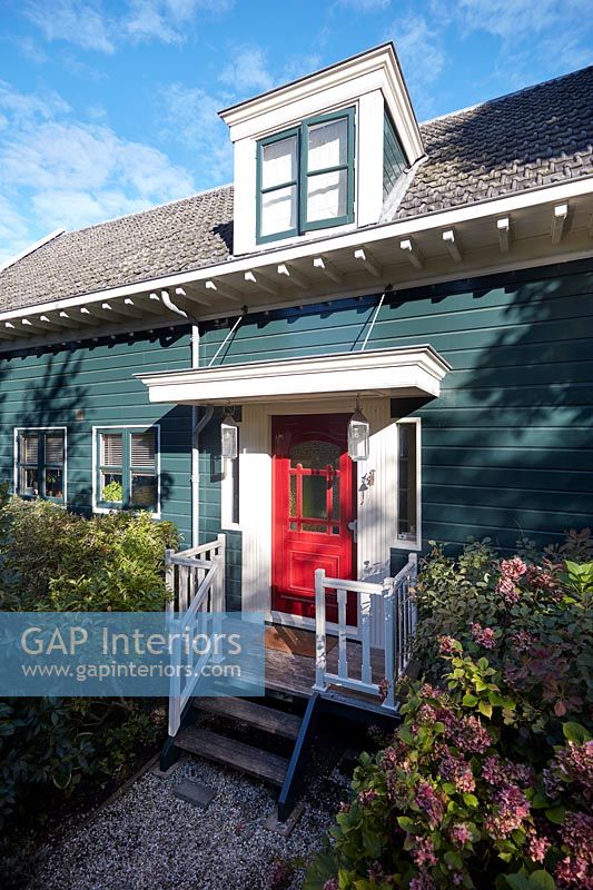 Teal painted wooden cottage exterior with red front door 