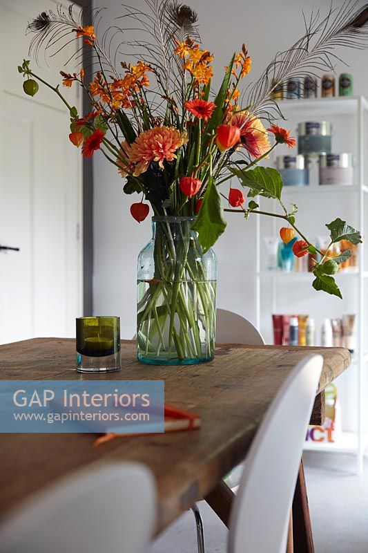 Red and orange cut flower arrangement in vase on dining table 