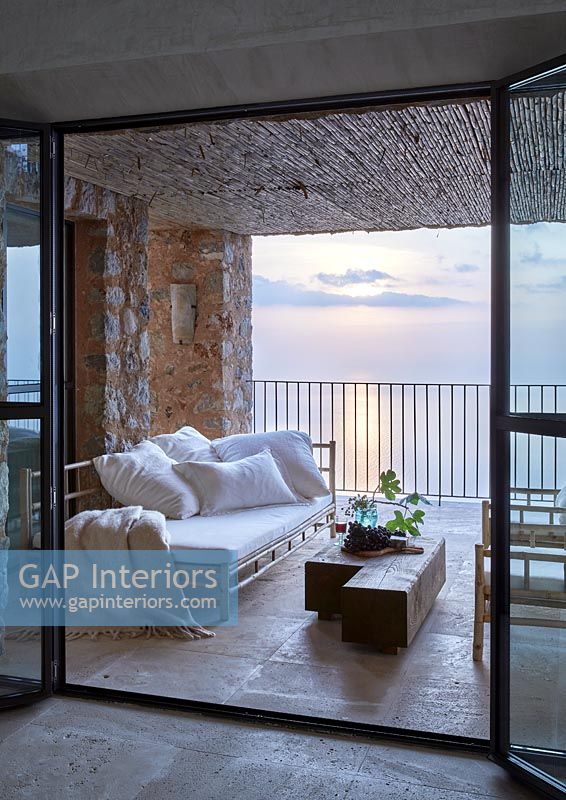 Day bed and armchairs on covered terrace overlooking the sea at sunset 