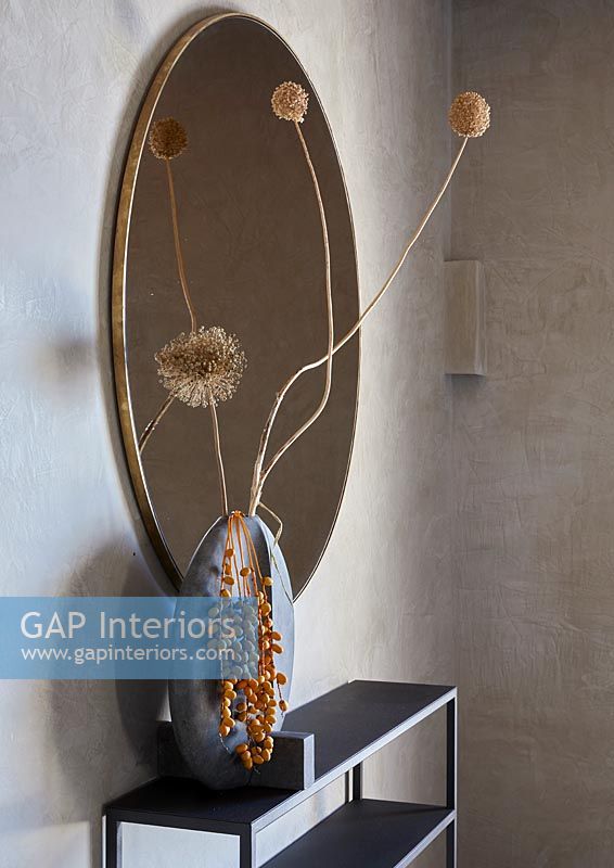 Detail of oval mirror and vase of dried flowers 