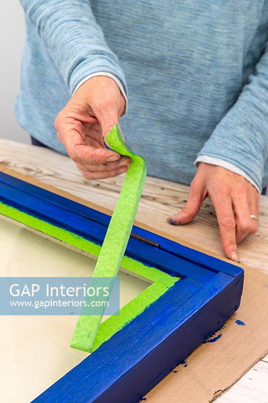 Woman peeling off protective tape after painting wooden frame
