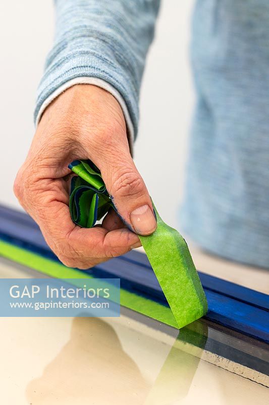 Woman peeling off protective tape after painting wooden frame
