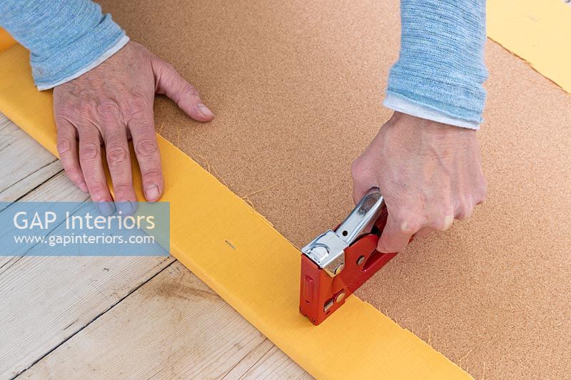 Woman stapling fabric to cork board - memories notice board craft project 