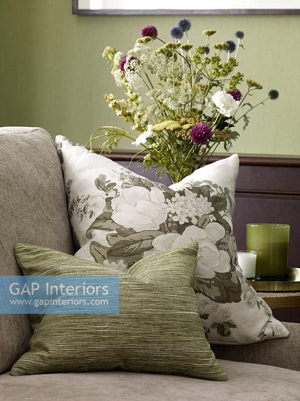 Floral cushion on sofa with flowers in vase behind 