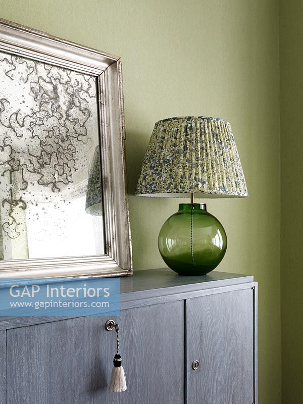 Green glass lamp on sideboard next to old mirror 