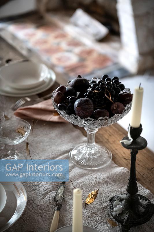 Dark coloured fruit in decorative glass bowl on dining table 