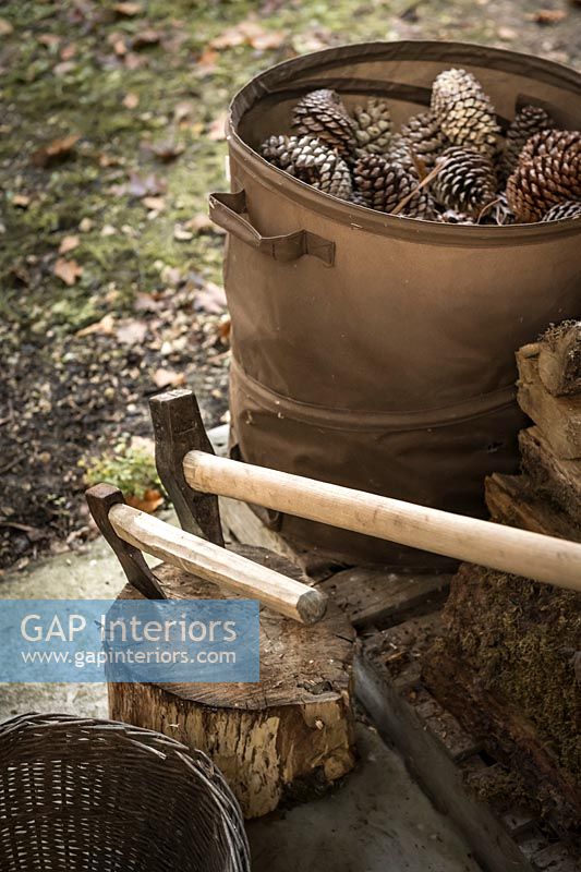 Axes in log next to basket of collected pinecones 