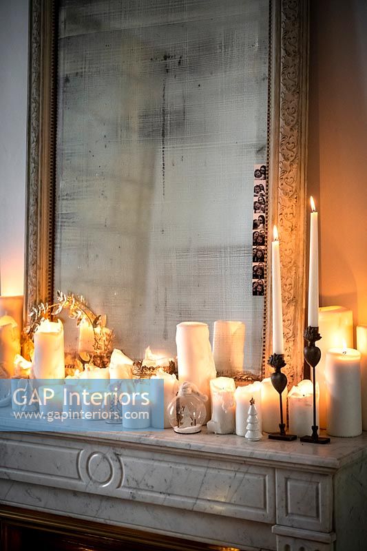 Display of lit candles in front of antique mirror on mantelpiece 