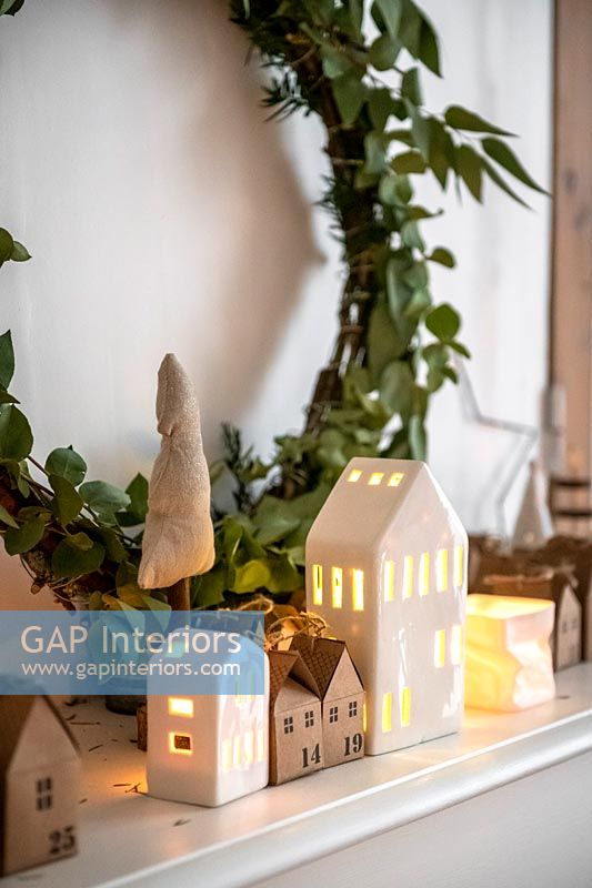 Wreath and tiny houses with candles in on mantelpiece at Christmas
