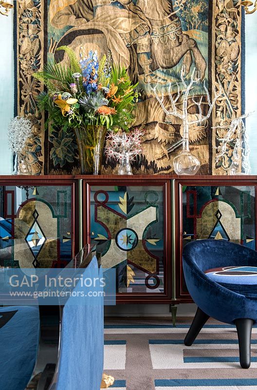 Glass fronted cabinet in front of large tapestry wall hanging 