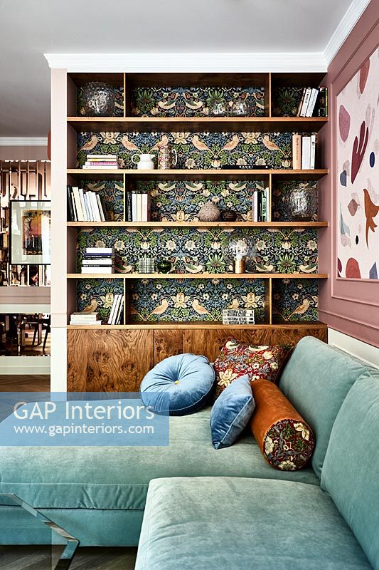 Modern living room with William Morris wallpaper behind shelving unit 