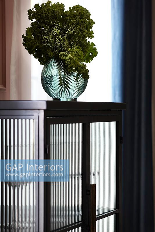 Decorative glass vase with kale leaves on black cabinet - detail 