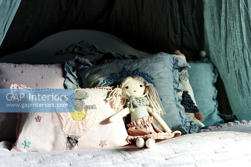 Detail of ragdoll and cushions on childs bed 
