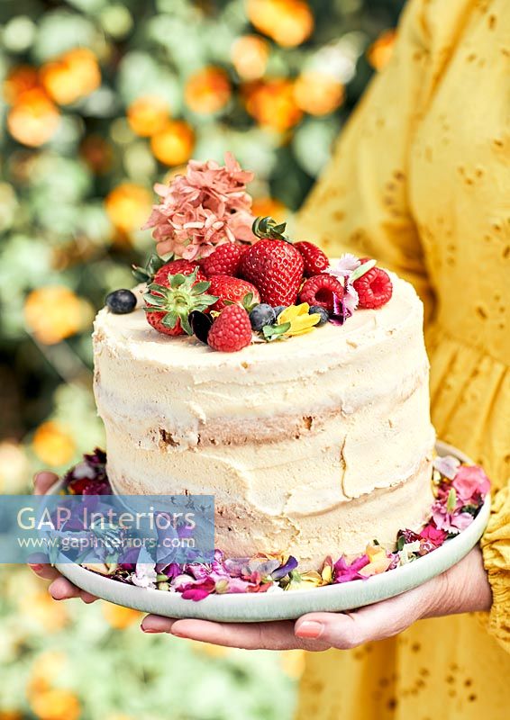 Woman holding celebration cake covered in fruit and flowers 