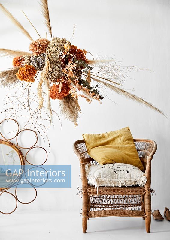 Dried flowers and grasses arrangement next to wicker chair 