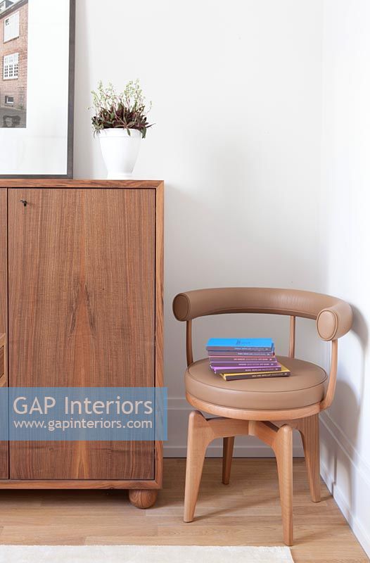 Small brown upholstered modern chair next to wooden sideboard 