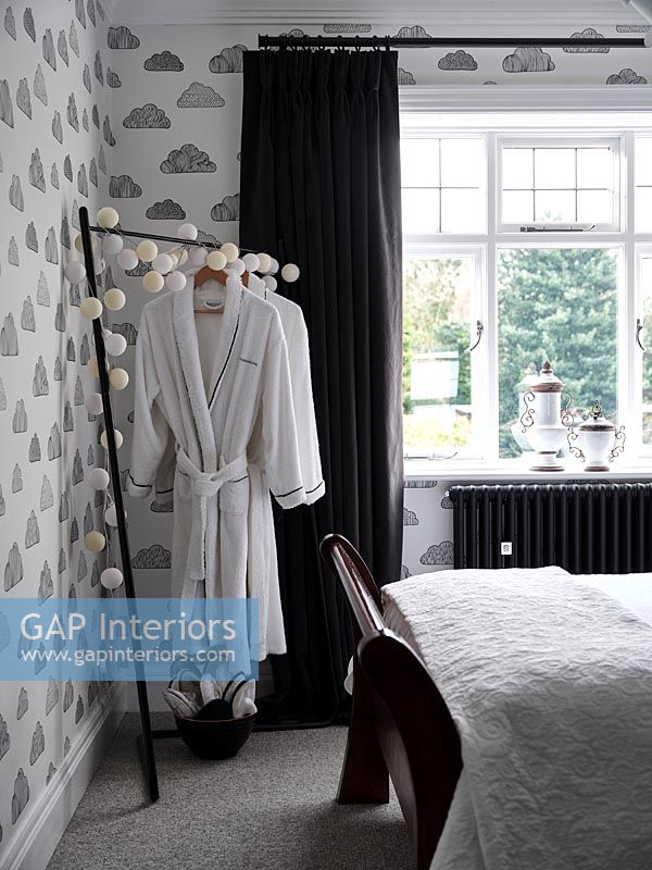 Towelling dressing gowns on rail in modern bedroom with cloud wallpaper 